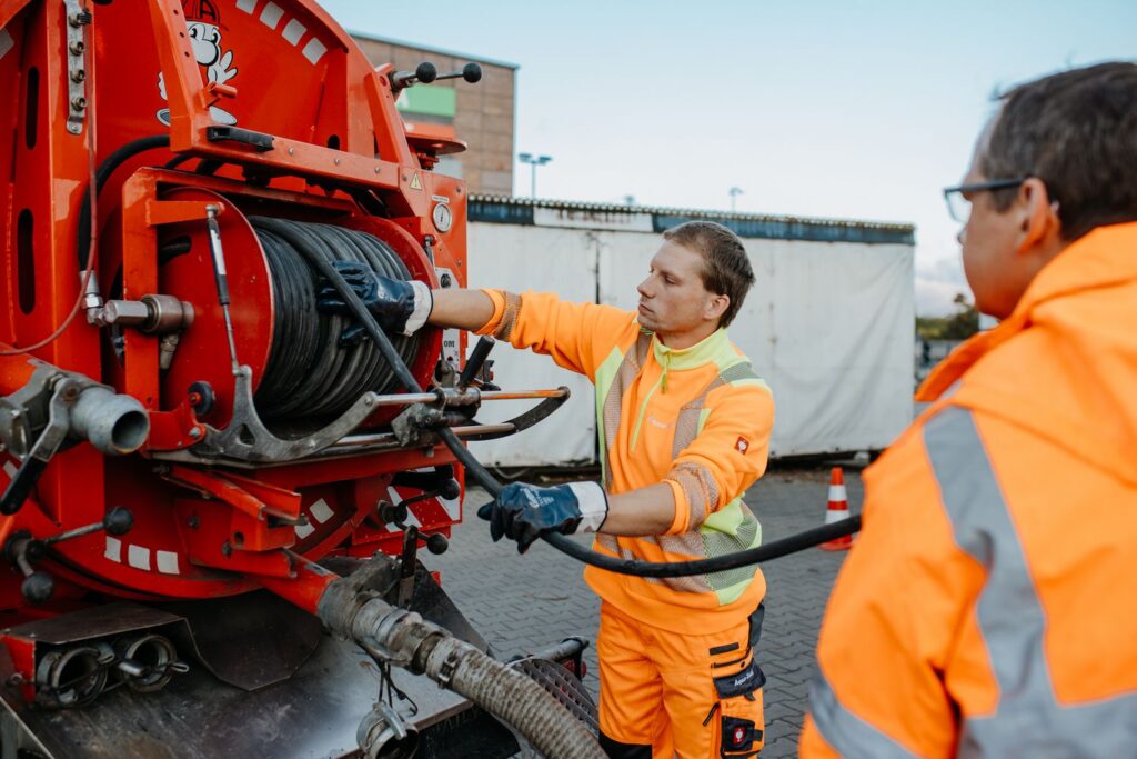 „AQUA-TOOL Fachkräfte bei der Druck- und Dichtheitsprüfung in Brandenburg: Mitarbeiter arbeiten mit Schlauch- und Prüftechnik am Spezialfahrzeug – Sicherheit für Entwässerungssysteme nach Norm.“
